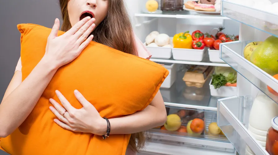 mulher segurando travesseiro em frente a geladeira aberta